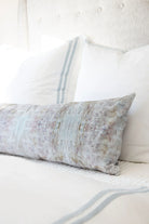 Luxury bolster pillow featuring an abstract garden-inspired pattern in layered bronze, iris blue, and earthy tones, styled for a collected modern traditional interior.